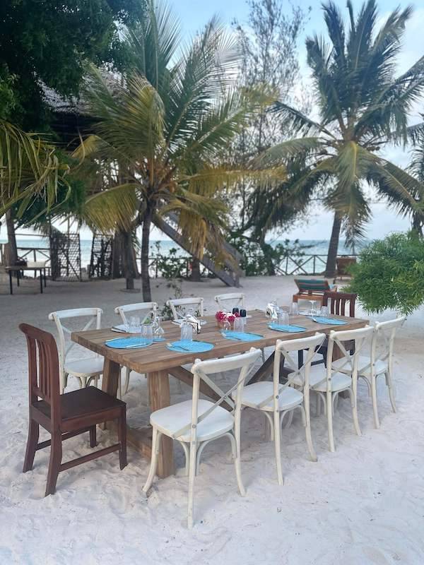 Long dinner table set on the sand under palms
